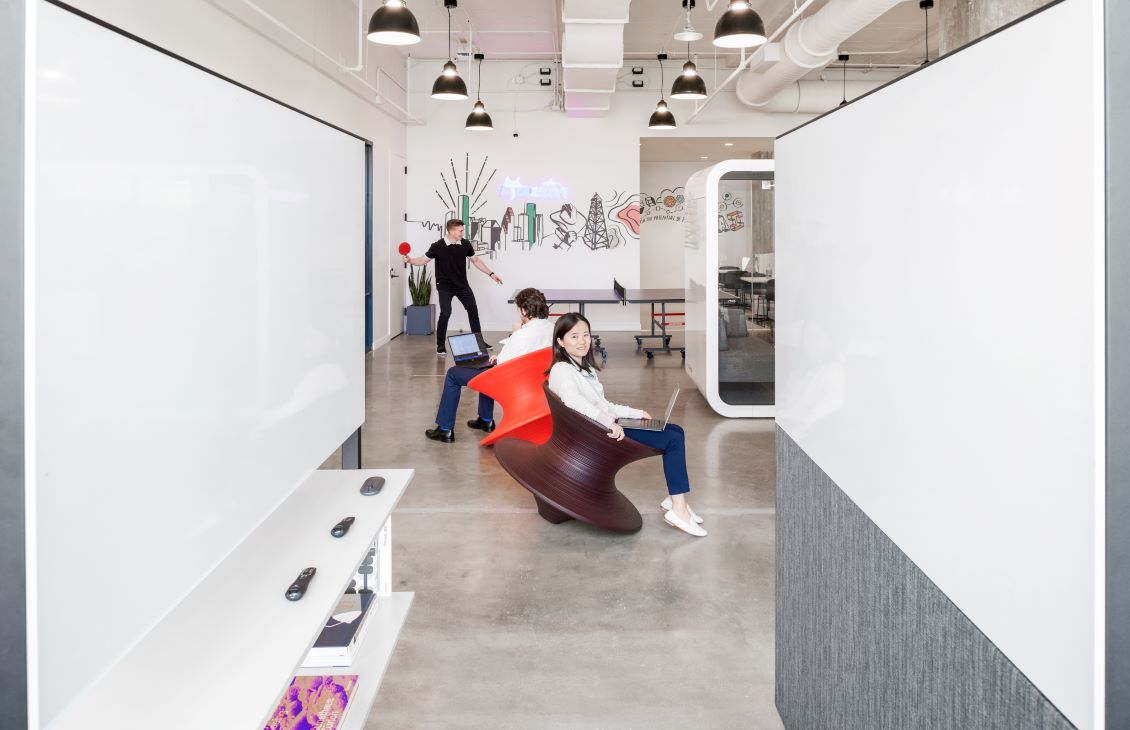 Three SLB employees, one throwing a ball, one sitting in a top chair and another working on a laptop