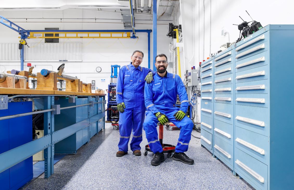 One SLB employee sitting on a red stool and another employee standing in coveralls