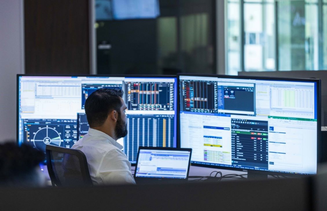 Man sitting at a computer with two large monitors in front of him