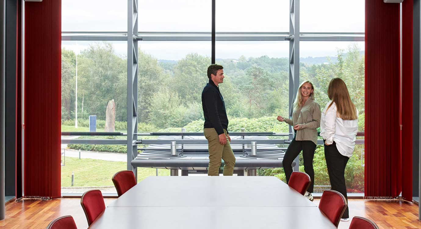 3 people having a meeting in a conference room in front of a large window.